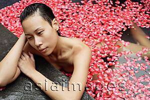 Asia Images Group - Woman leaning at edge of tub filled with floating rose petals