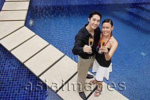 Asia Images Group - Couple standing by swimming pool, looking up at camera, holding champagne glasses