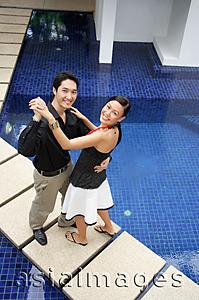 Asia Images Group - Couple dancing by swimming pool, smiling at camera