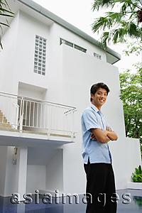 Asia Images Group - Man standing outside house, arms crossed