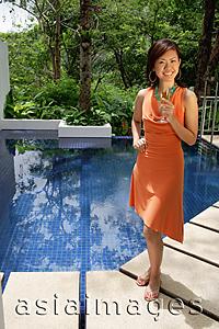 Asia Images Group - Woman standing by swimming pool, holding glass of champagne