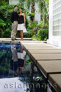 Asia Images Group - Couple standing by swimming pool, smiling at camera