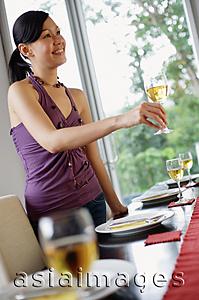Asia Images Group - Young woman standing next to set dining table, holding glass of wine