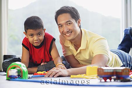 Asia Images Group - Father and son side by side on floor, smiling at camera, train set in front of them
