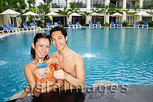 Asia Images Group - Couple in swimming pool, holding cocktails, smiling at camera