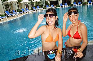 Asia Images Group - Young women in swimming pool, lifting sunglasses, smiling