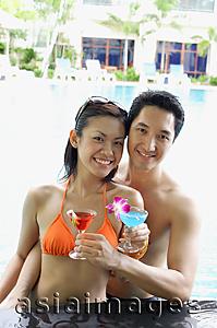 Asia Images Group - Couple in swimming pool holding cocktail drinks, smiling at camera