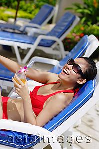 Asia Images Group - Woman in bikini, sitting on deck chair, holding drink, smiling