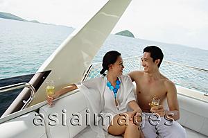 Asia Images Group - Couple sitting on stern of yacht, holding champagne glasses
