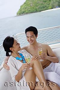 Asia Images Group - Couple sitting on stern of yacht, with champagne glasses