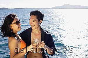 Asia Images Group - Couple holding champagne glasses, toasting, ocean behind them