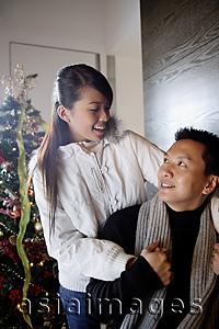 Asia Images Group - Couple in winter wear looking at each other, Christmas tree behind them