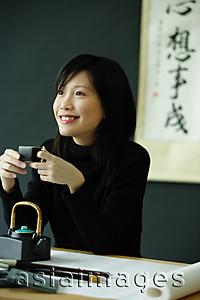 Asia Images Group - Young woman holding Chinese teacup, smiling, looking away