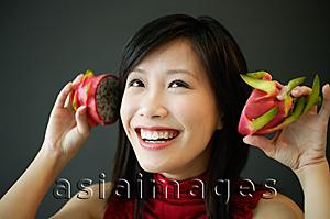 Asia Images Group - Woman holding dragon fruit halves next to her ears, smiling