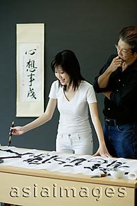 Asia Images Group - Woman painting Chinese calligraphy, man next to him watching