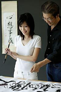 Asia Images Group - Woman holding paintbrush, looking at Chinese painting, man standing next to her
