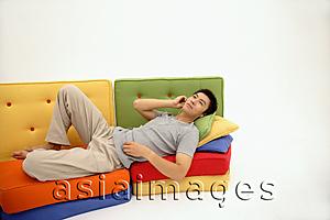 Asia Images Group - Man lying on multi-coloured sofa, listening to personal stereo