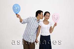 Asia Images Group - Couple holding hands, holding balloons, man leaning over to kiss woman on cheek