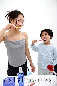 Asia Images Group - Mother and young daughter brushing teeth, looking at each other