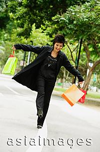 Asia Images Group - Woman dressed in black, holding shopping bags, walking on road