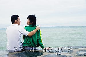 Asia Images Group - Couple sitting on breakwater, embracing, rear view