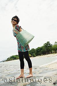 Asia Images Group - Woman standing on beach, carrying beach bag