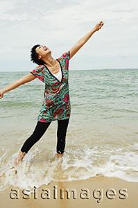Asia Images Group - Woman standing in sea, looking up, arms outstretched