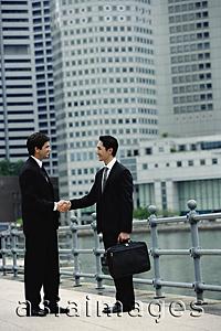Asia Images Group - Two businessmen shaking hands, river and buildings in the background