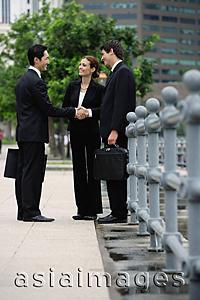 Asia Images Group - Business people standing in the city, shaking hands, buildings in the background