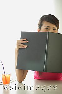 Asia Images Group - Woman sitting at cafe table, holding menu over her face