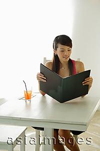 Asia Images Group - Woman sitting at cafe table, holding menu