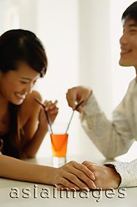 Asia Images Group - Couple sharing drink, sitting face to face, holding hands