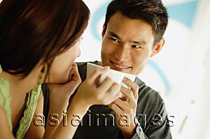 Asia Images Group - Couple drinking from cups, looking at each other