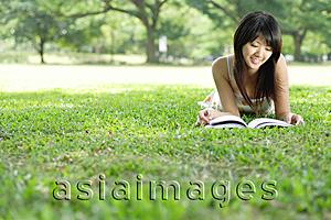 Asia Images Group - Young woman lying on grass in park, looking at magazine