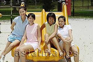 Asia Images Group - Young women sitting on slide in playground, smiling at camera