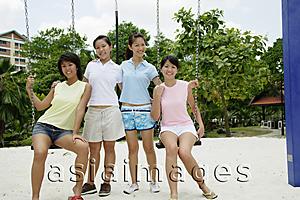 Asia Images Group - Young women in playground, sitting on swings, smiling at camera
