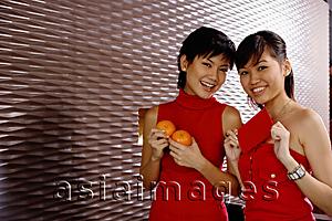Asia Images Group - Young women dressed in red, holding two oranges and red packet
