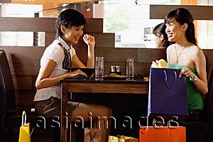 Asia Images Group - Young women in restaurant, looking at shopping bags