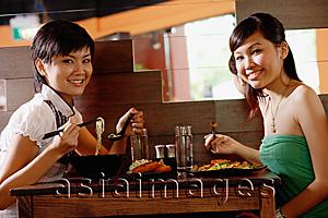 Asia Images Group - Two young women sitting at table in restaurant, smiling at camera