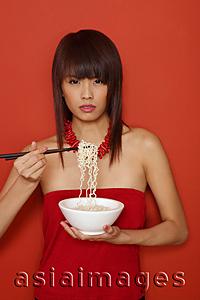 Asia Images Group - Young woman in red, holding bowl of noodles, looking at camera