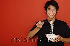 Asia Images Group - Man standing against red wall, holding bowl of noodles