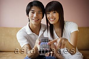 Asia Images Group - Couple on sofa, holding TV remote control