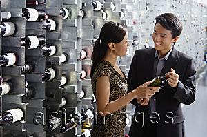 Asia Images Group - Couple in wine cellar, studying bottle of wine