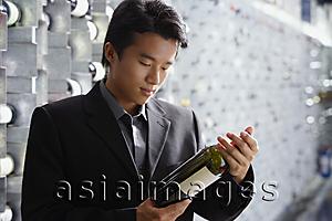 Asia Images Group - Man in wine cellar, looking at bottle of wine