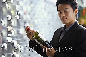 Asia Images Group - Man in wine cellar, holding bottle of wine