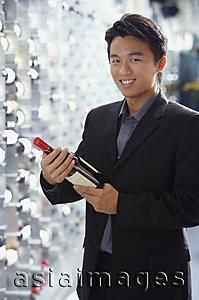 Asia Images Group - Man in wine cellar, holding bottle of wine, smiling at camera
