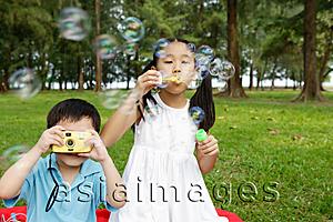 Asia Images Group - Girl blowing bubbles, boy taking pictures with camera