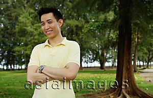 Asia Images Group - Man standing in park, smiling at camera, arms crossed