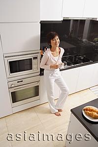 Asia Images Group - Young woman standing in kitchen, looking at camera, smiling