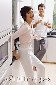 Asia Images Group - Couple standing in kitchen, having coffee, looking at camera